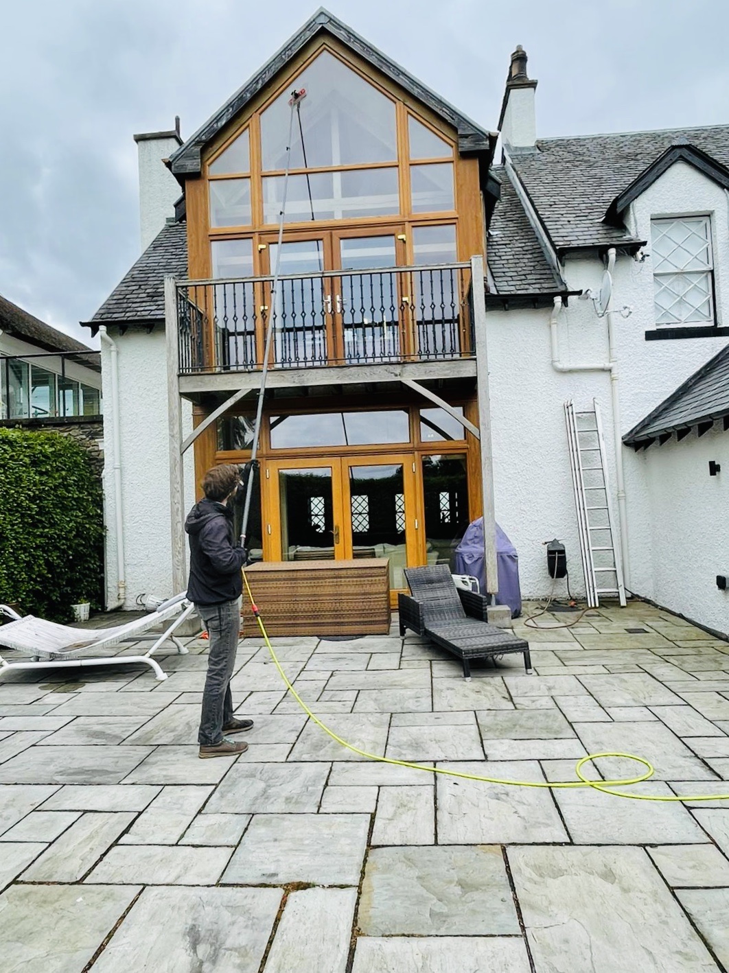 Nathaniel cleaning the tall glazed gable of a whitewashed house with a water-fed pole