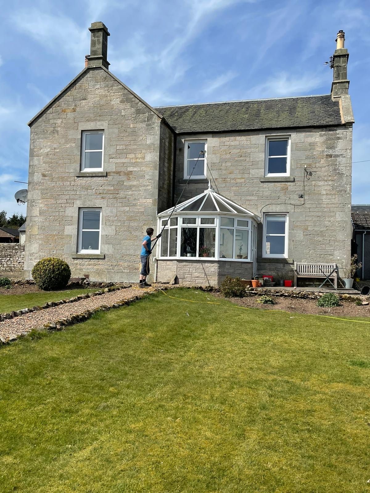 A stone farmhouse with a conservatory, Nathaniel cleaning the upstairs windows from the lawn