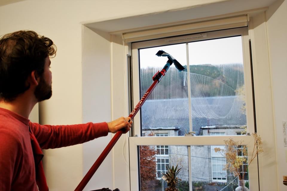 Nathaniel cleaning a sash window from inside with a pole, Borders hillside outside