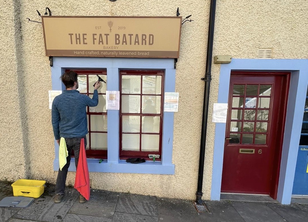 Nathaniel squeegeeing the windows of The Fat Batard Bakery shopfront