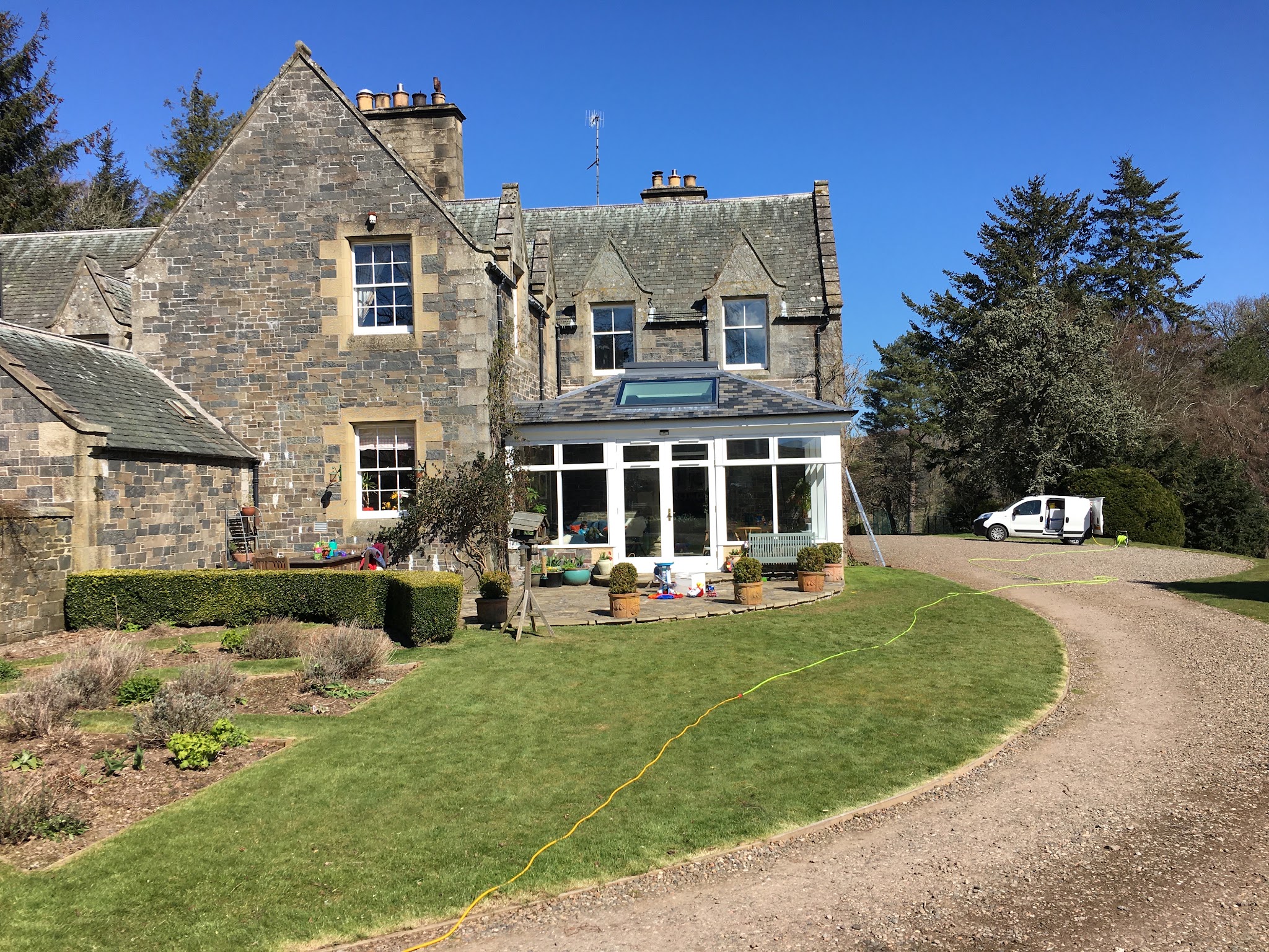 A large stone house with a conservatory and gravel drive, the van parked by the door